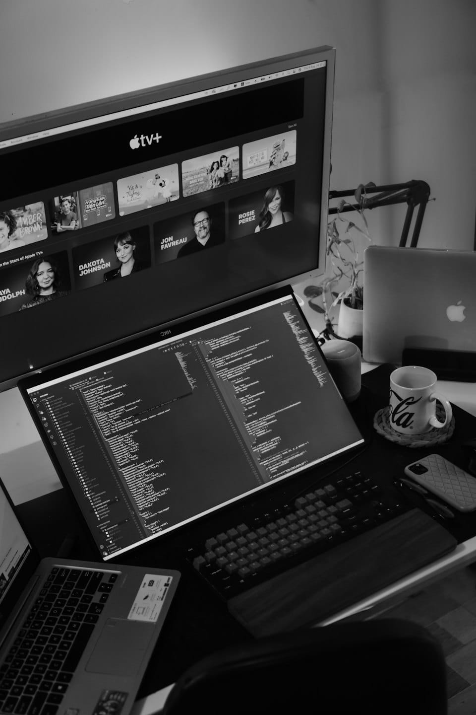 Nowoczesne biurko z dwoma monitorami wyświetlającymi kod i serwis streamingowy.
